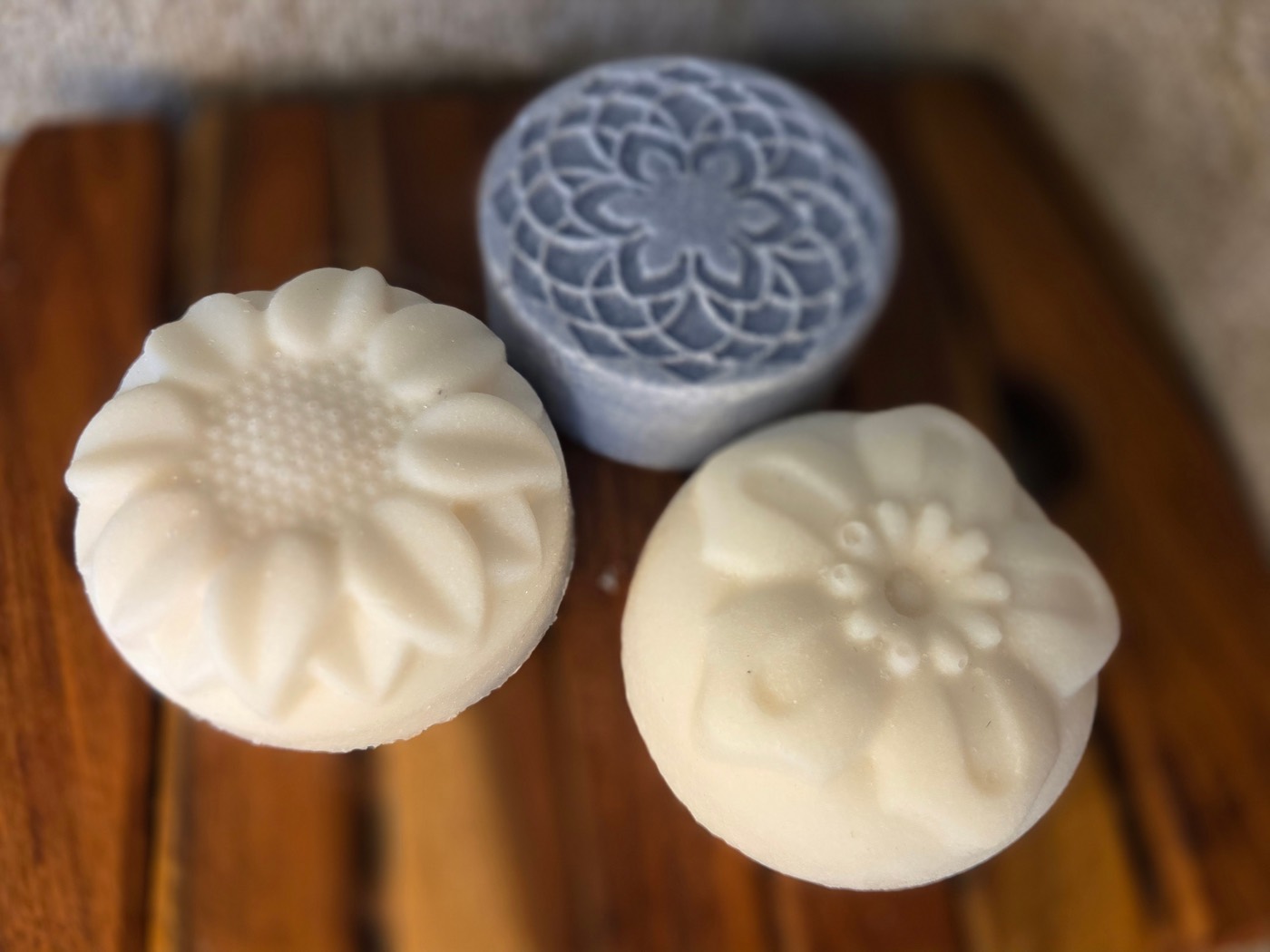 Two white flower-molded salt soap rounds with a blue mandala round behind